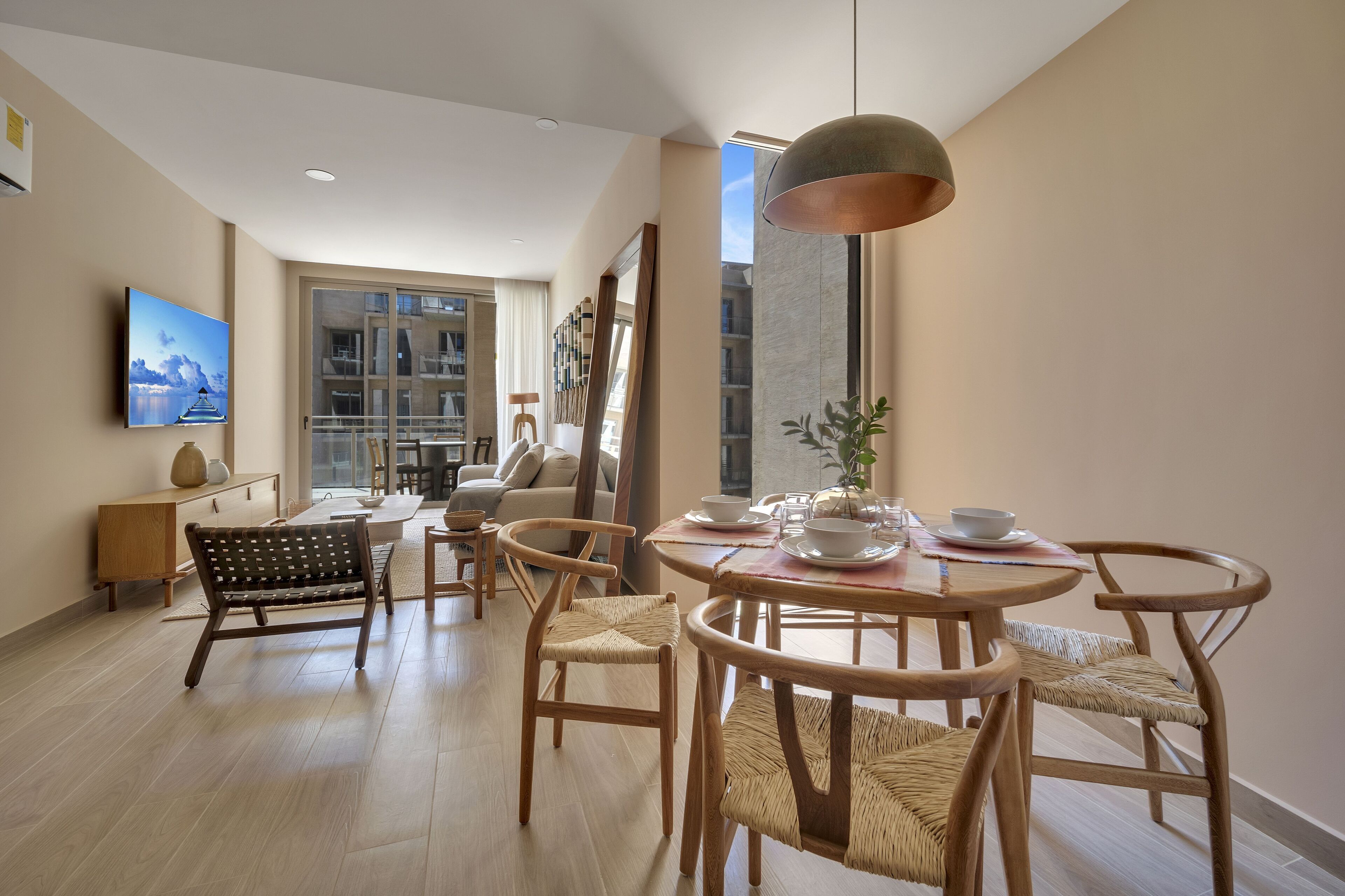 Ein modernes Wohnzimmer mit einem runden Esstisch, Korbstühlen, einer Couch und einem großen Fenster mit Blick auf die Stadt.