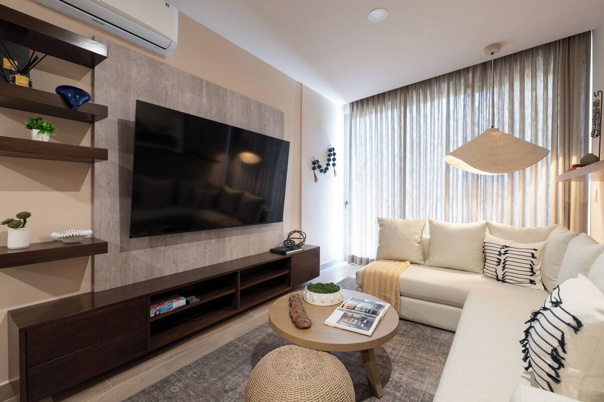 A modern living room with a large flat-screen TV, a sofa, a coffee table, and a TV stand with shelves.