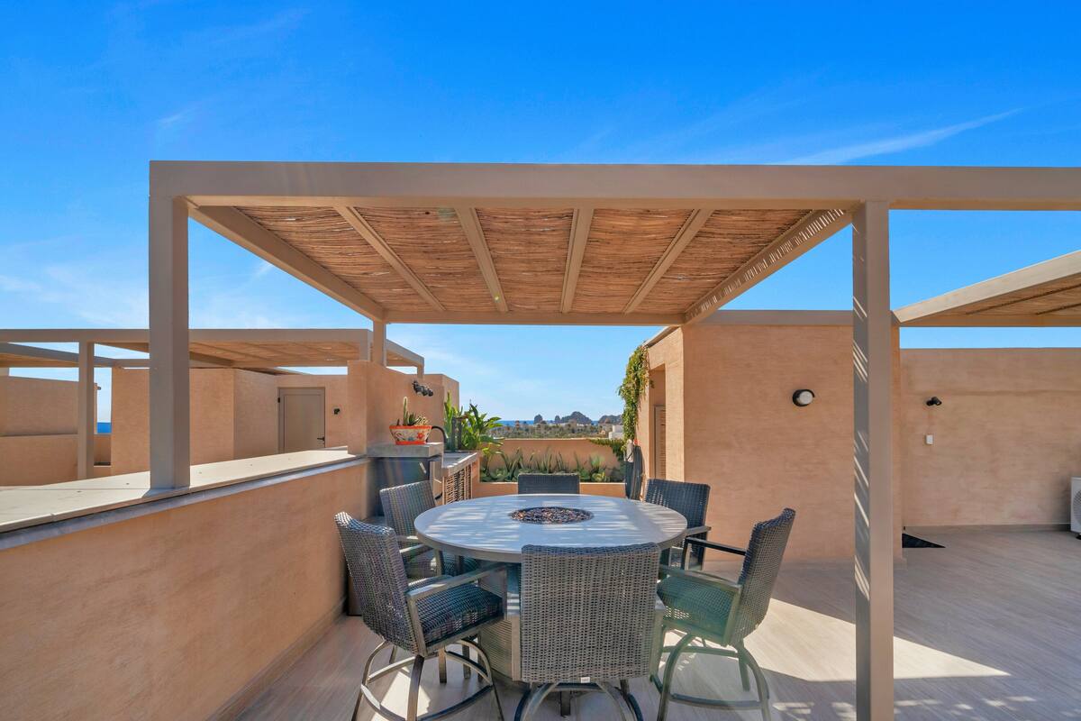 An outdoor patio with a round table and chairs, a pergola overhead, and a view of the landscape.