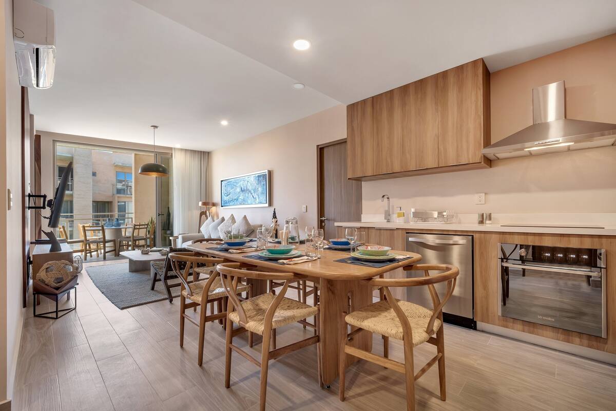 A modern kitchen with wooden cabinets, stainless steel appliances, and a dining area with wicker chairs.