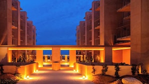 Un hôtel moderne à l’architecture symétrique, doté d’une cour intérieure avec des espaces pour s’asseoir et des plantes, et d’un éclairage d’ambiance nocturne.