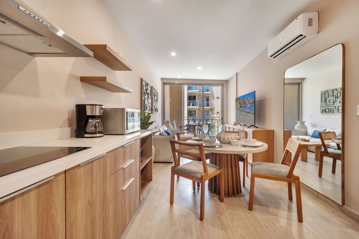 A modern kitchen with wooden cabinets, a built-in oven, and a dining area with a round table and chairs.