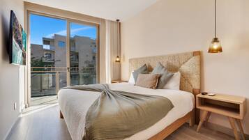Une chambre moderne avec un grand lit, une table de chevet en bois, une lampe suspendue et une vue sur les immeubles par une grande fenêtre.