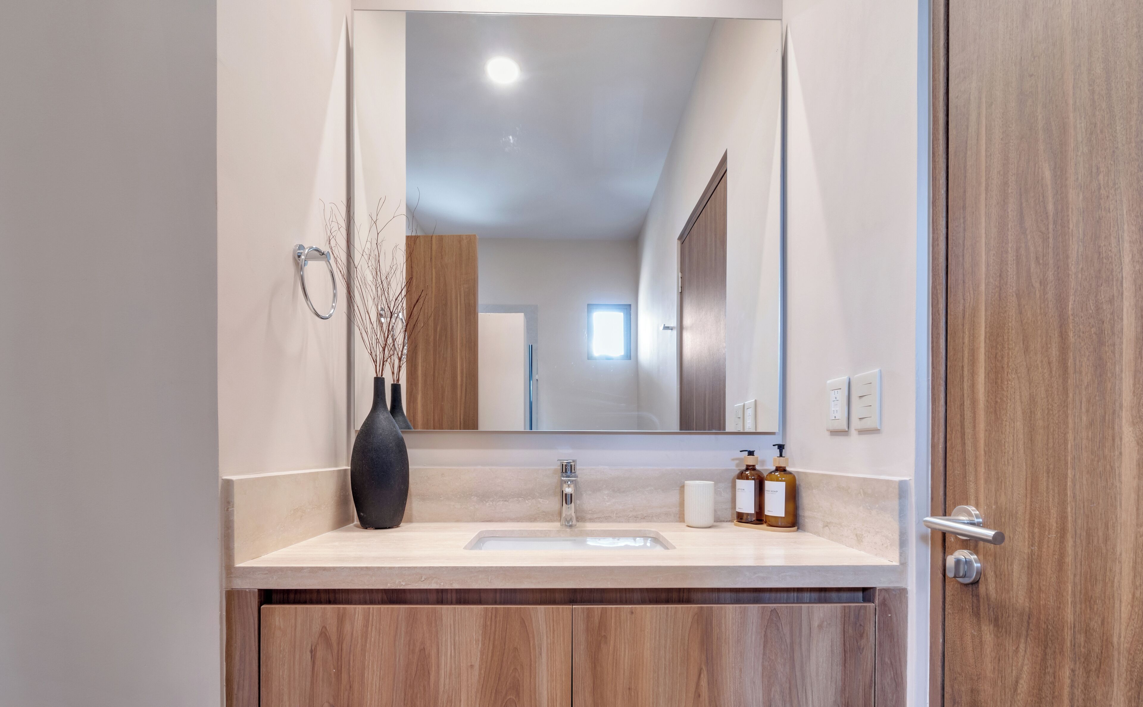 A modern bathroom with a large mirror, a sink, and wooden cabinets.