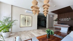 Una sala de estar moderna con una mesa de centro de madera, un sofá y un cuadro abstracto grande. Hay un mostrador de recepción con un panel de pared de madera y un letrero que dice