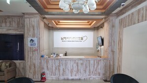 A reception desk with a sign reading "Namha Beach Pension Hotel" and a "Best" award sign. There are two wicker chairs and a fire extinguisher on the floor. - Namhae beach hotel (Namhae)