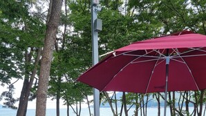 A wooden deck with a barbecue grill, picnic table, and umbrella. - Namhae beach hotel (Namhae)