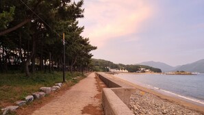 A paved pathway beside a pebble beach with a concrete barrier, leading to a body of water. - Namhae beach hotel (Namhae)