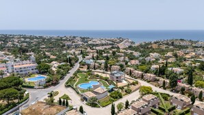 An aerial view of a residential area with a large swimming pool complex, surrounded by houses and greenery.