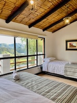 Una habitación con un ventanal grande, una cama, una mesita de noche y una lámpara colgante.