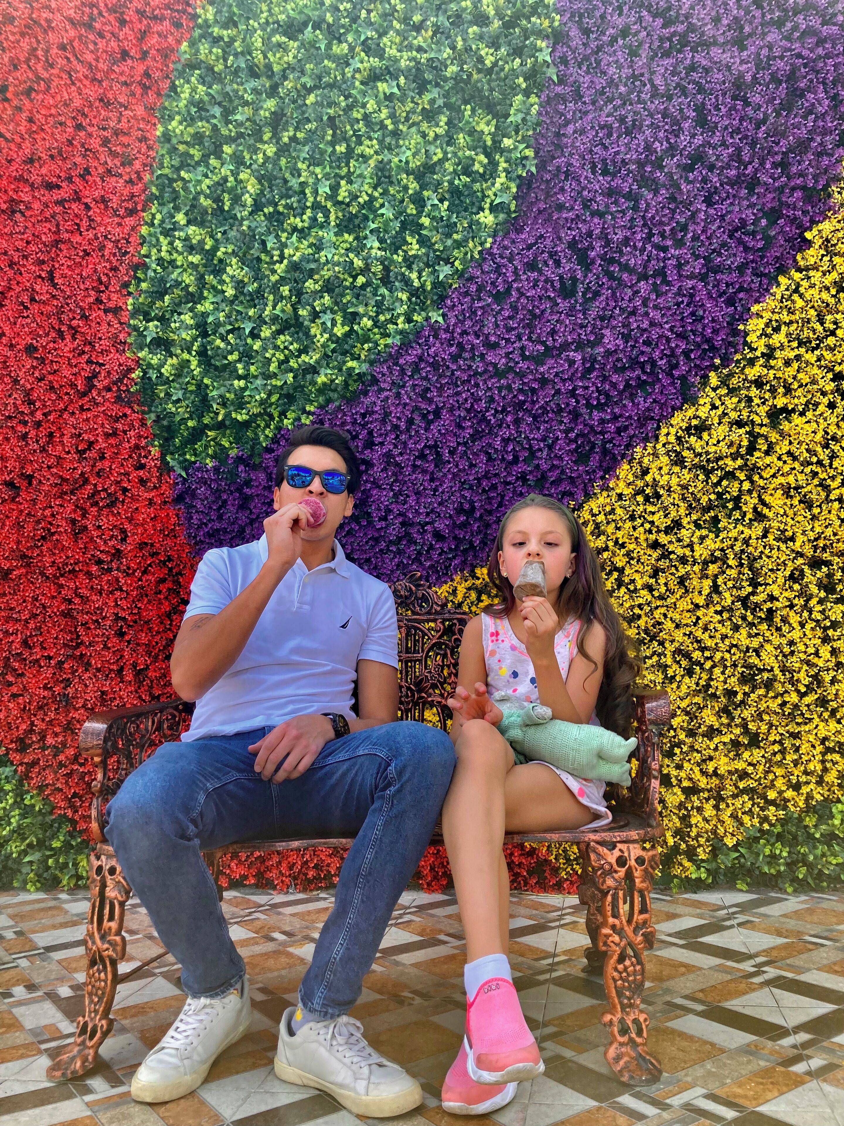 Un hombre y una mujer sentados en un banco con un fondo floral colorido.