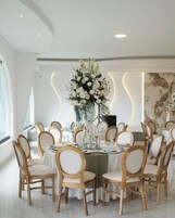 Un comedor con mesas redondas, sillas de madera y un gran centro de mesa floral.
