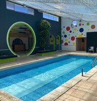 Una piscina interior con suelo de baldosas, una estructura circular verde y una pared con diseños circulares de colores.