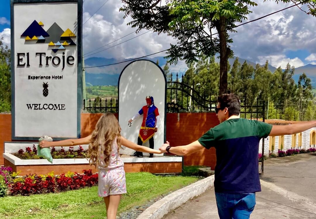 A welcome sign at El Troje Experience Hotel with a statue of a figure in a blue and red outfit.