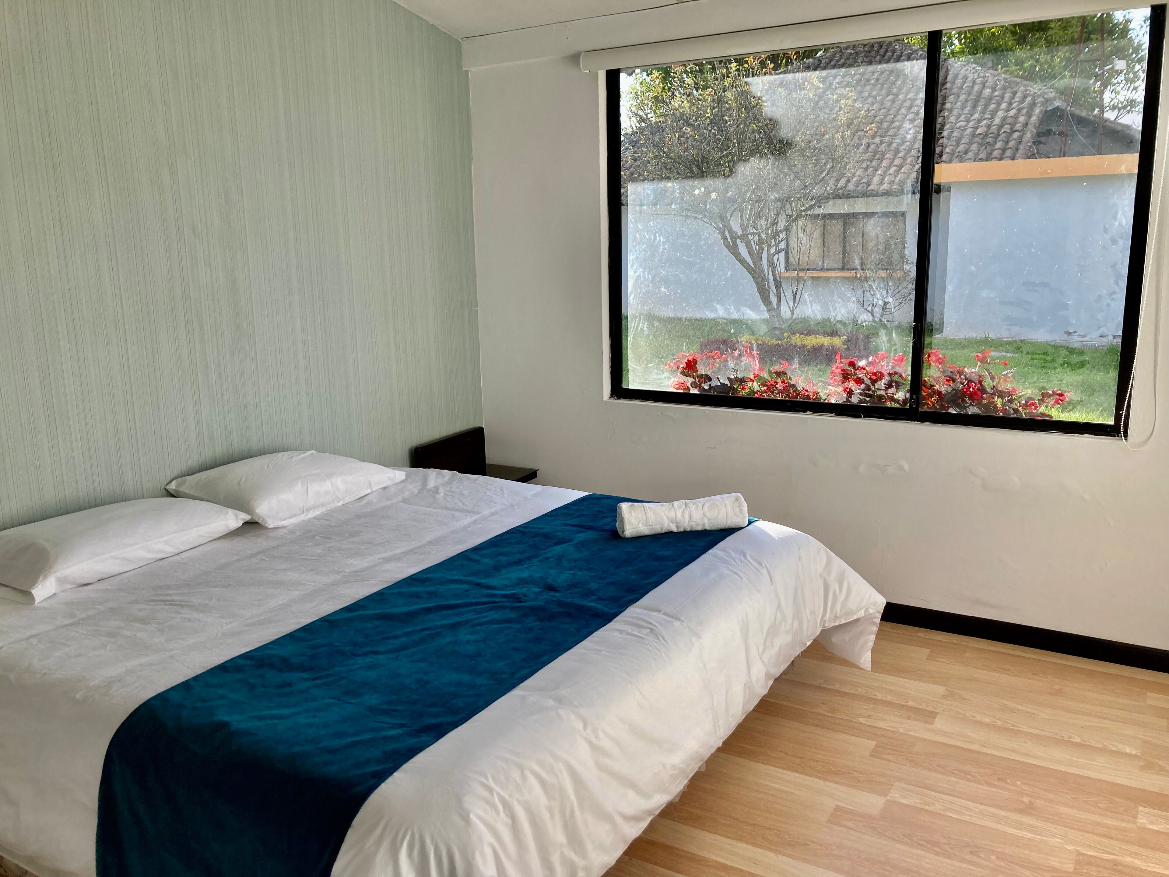 Un dormitorio con cama, mesita de noche y ventana con vistas a un jardín.