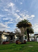 Una casa con fachada de piedra, techo de tejas y un jardín bien cuidado con una palmera.