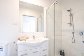 Een moderne badkamer met een wit wastafelmeubel, spiegel en een douchecabine van glas.