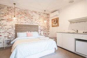 Een slaapkamer met een baksteenmuur, een bed met wit beddengoed, een nachtkastje en een kleine witte stoel.