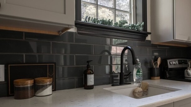 A kitchen with a black backsplash, white countertops, a black faucet, and a window with greenery above the sink. - The Safe Harbor Home | Quiet Retreat, Fire Pit, Nature (Conestoga)