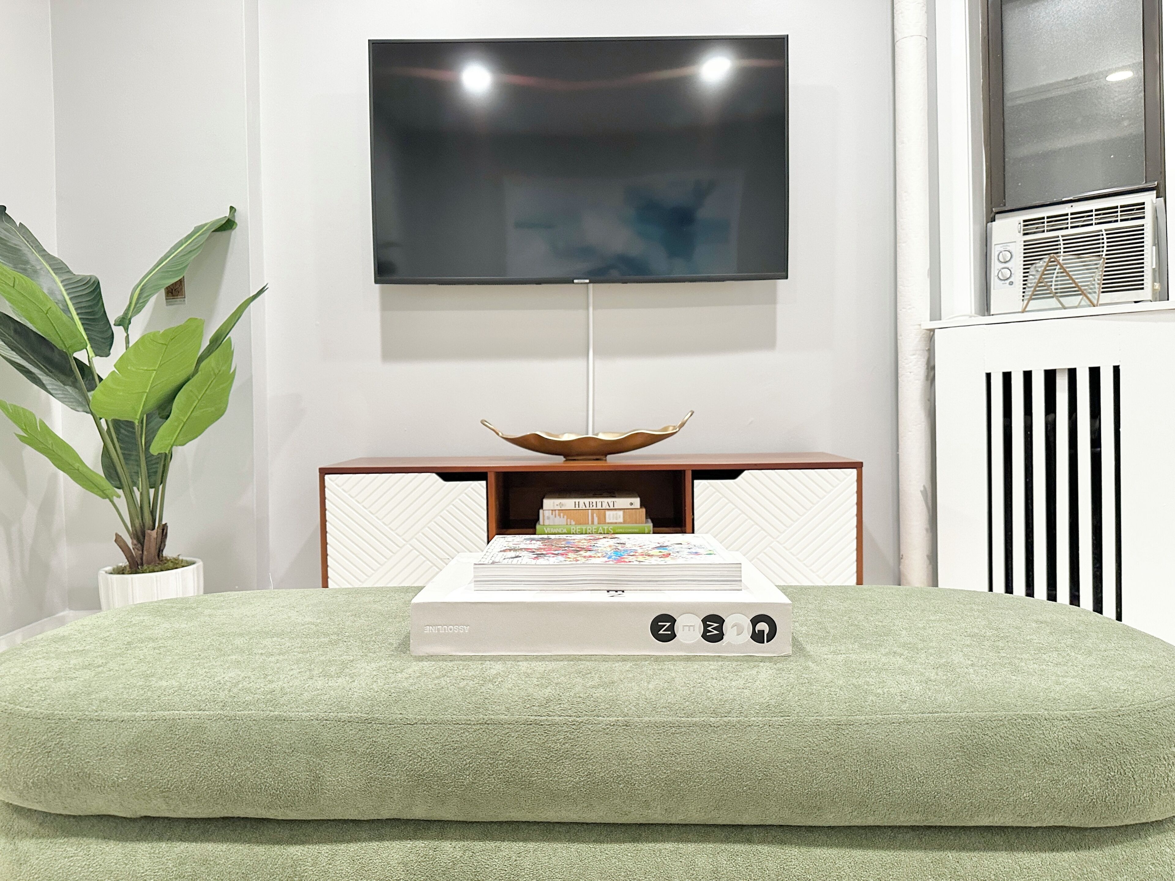 A modern living room with a flat-screen TV mounted on the wall, a decorative bowl on a wooden console table, and a radiator on the right.