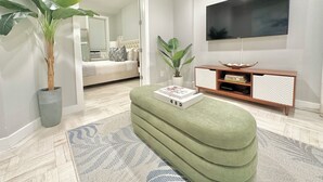 A modern living room with a green sofa, a flat-screen TV, and a potted plant.