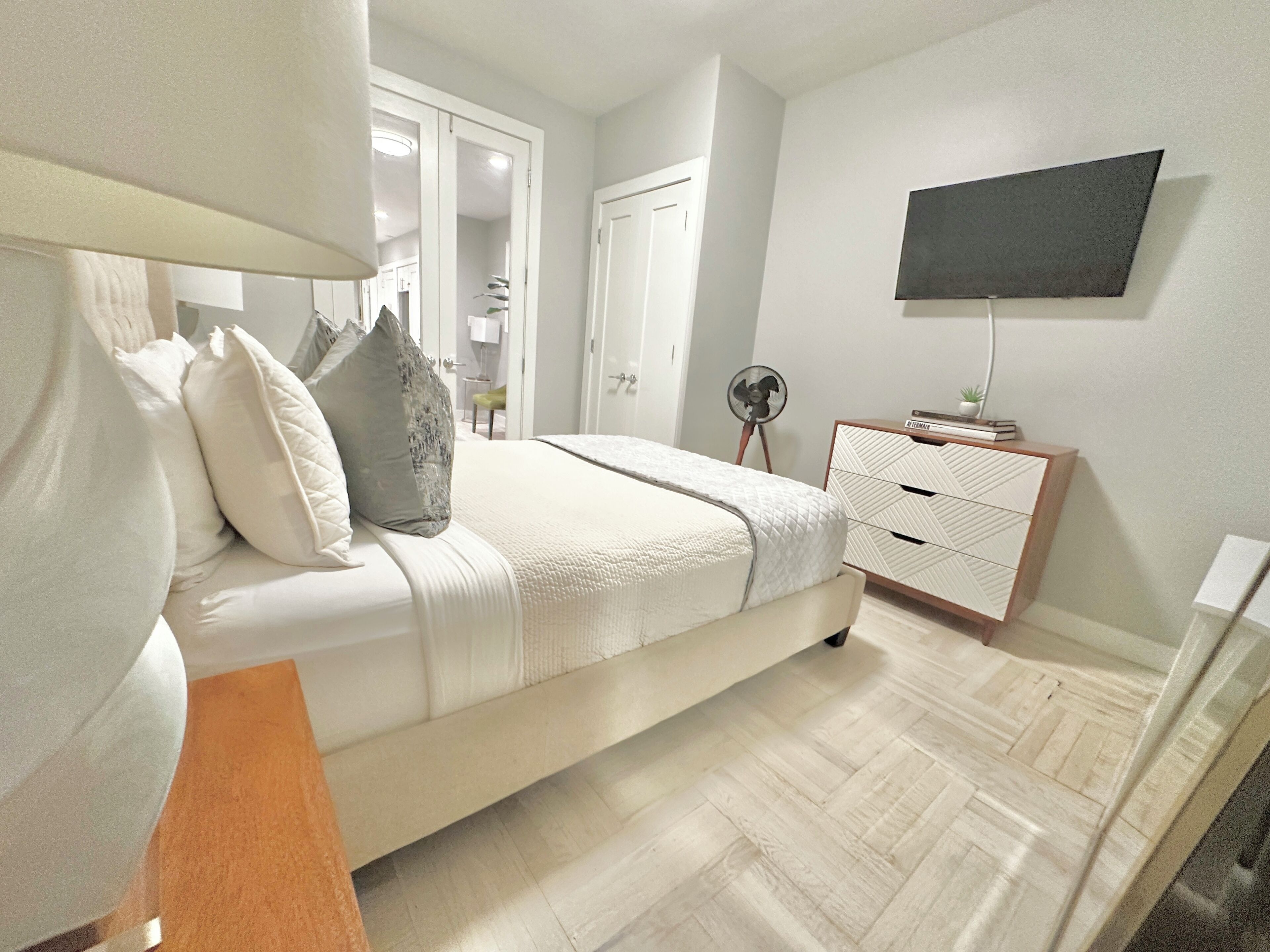 A bedroom with a bed, bedside table, dresser, and a TV mounted on the wall.