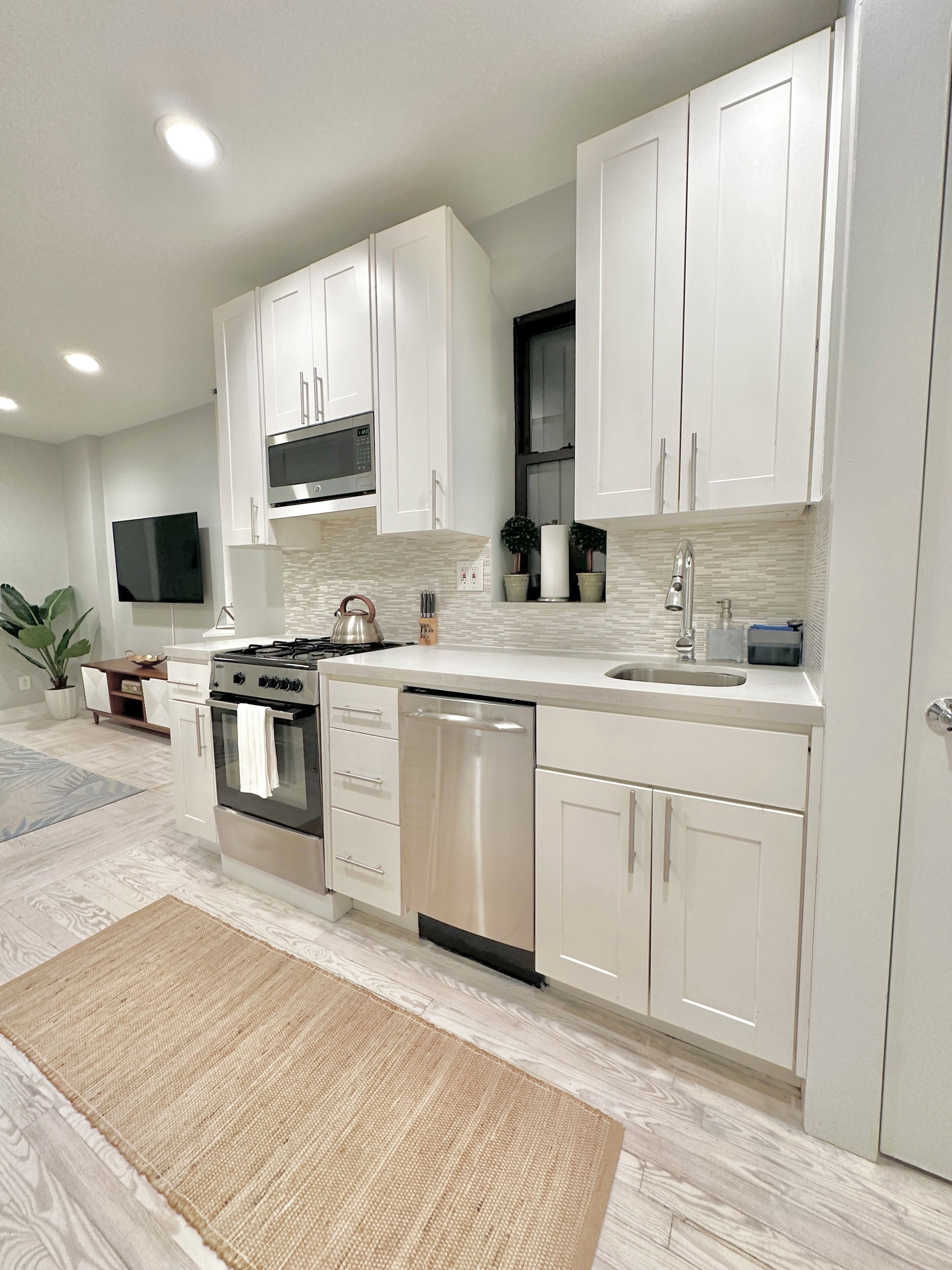 A modern kitchen with white cabinets, stainless steel appliances, a built-in microwave, and a large window above the sink.