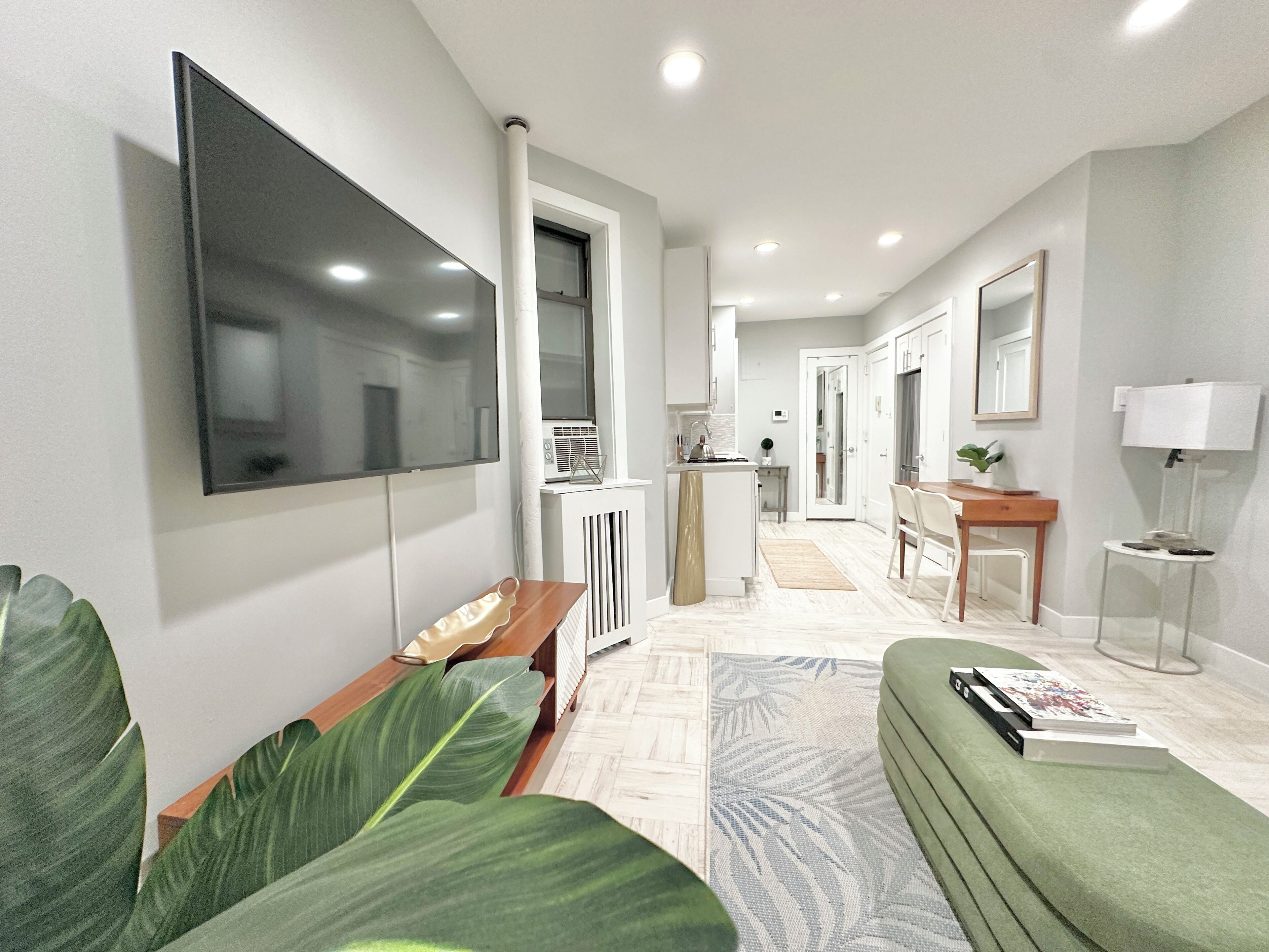 Una sala de estar moderna con un televisor de pantalla plana, un sofá, una mesa de centro y una planta verde grande.