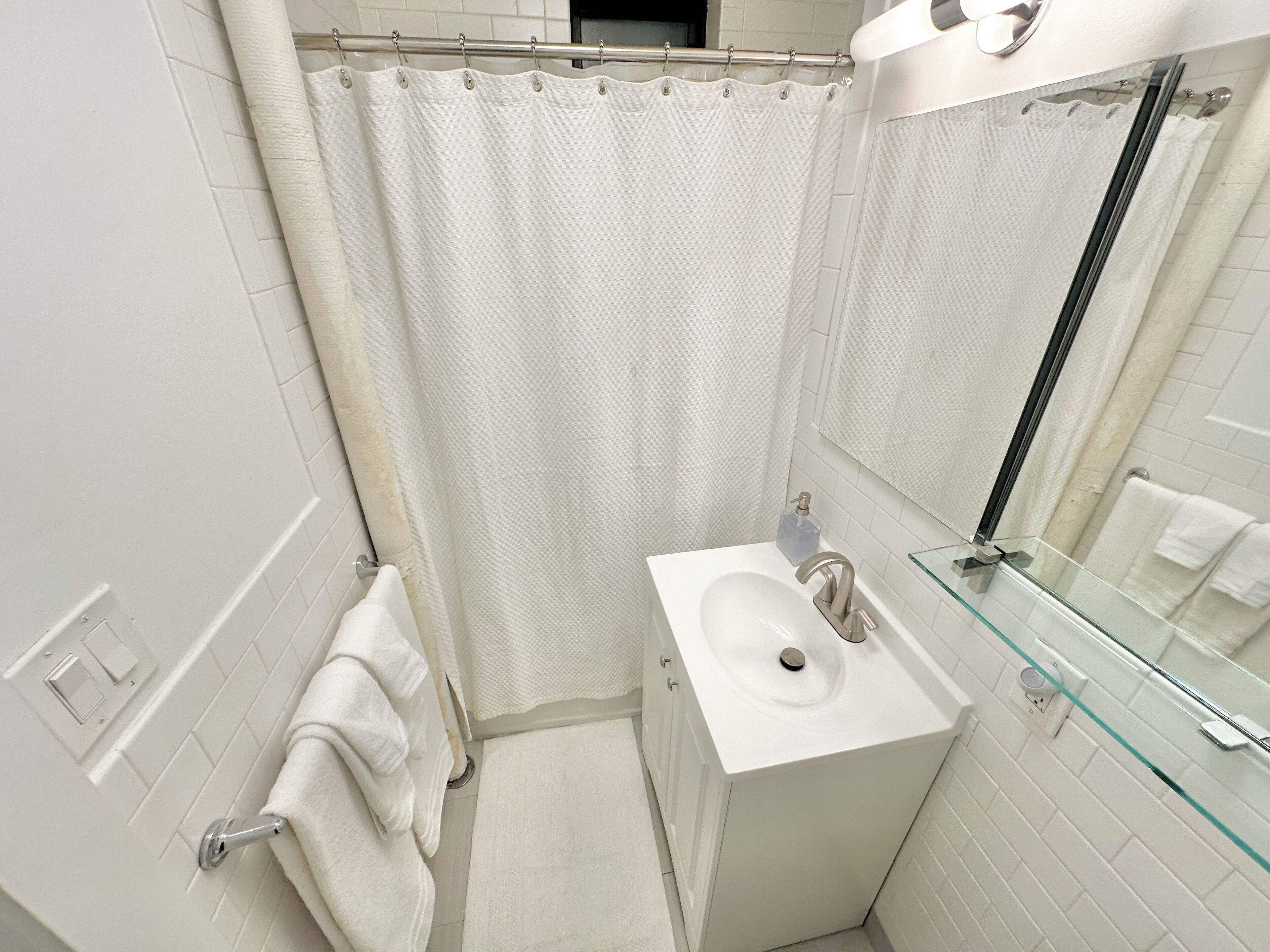 A modern bathroom with a white sink, glass shower enclosure, and a towel rack.