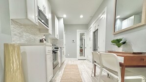 A modern kitchen with white cabinetry, a built-in oven, and a wooden dining table with chairs.