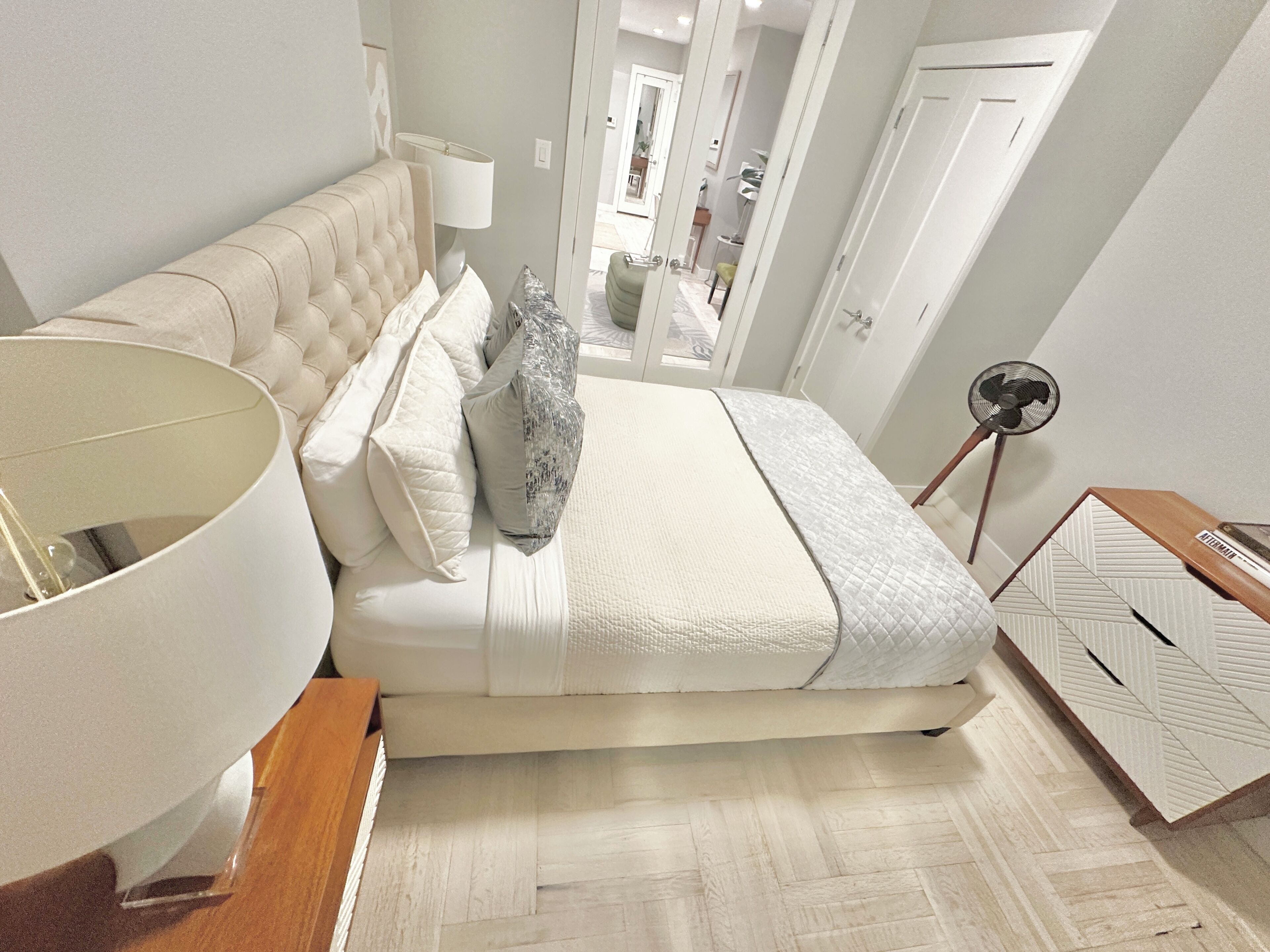 Un dormitorio con una cama, una mesita de noche con lámpara, un ventilador y un espejo.