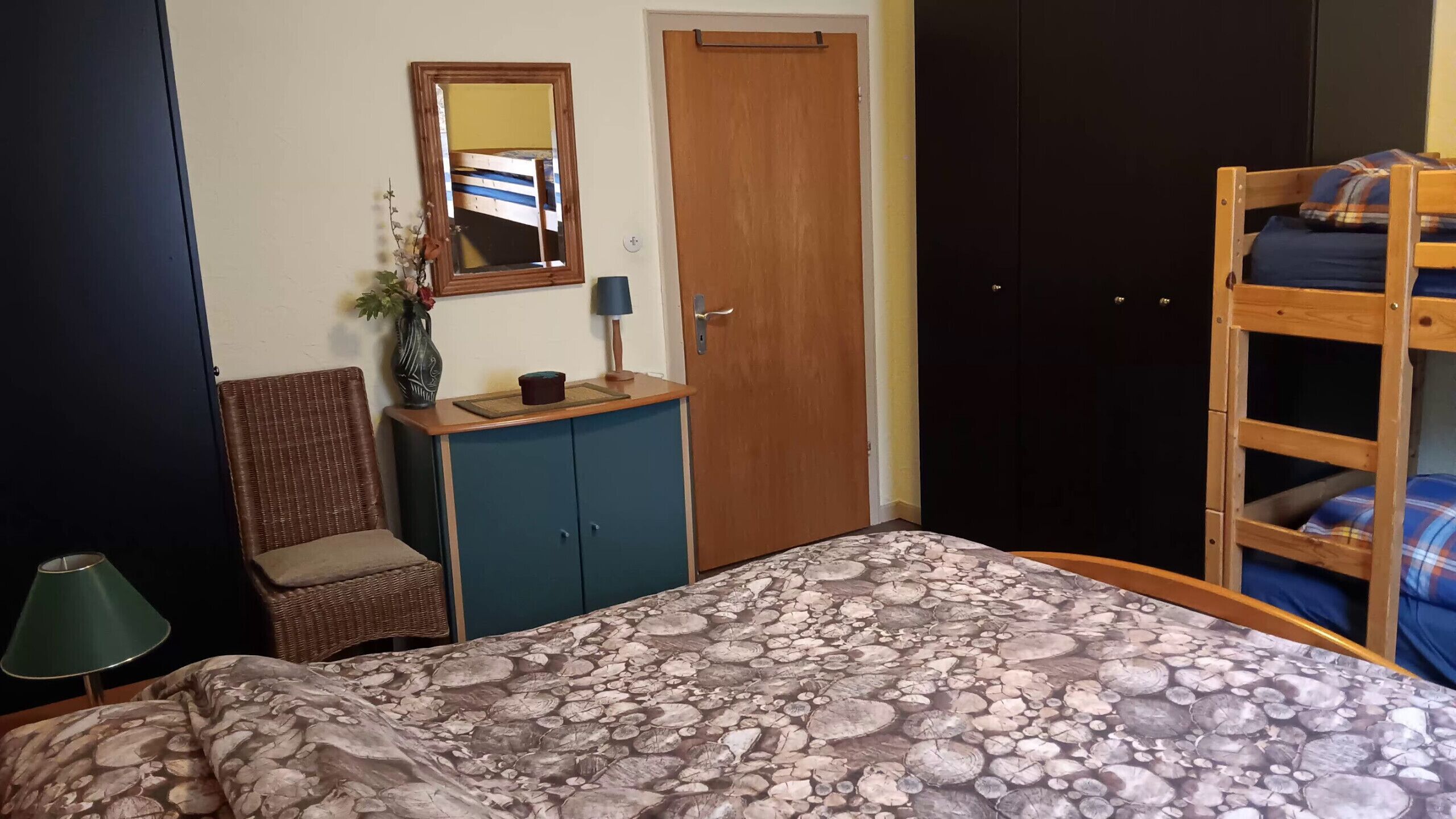 Un dormitorio con una cama litera, una silla, un aparador, un espejo y una puerta.