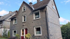 A two-story house with a red door, multiple windows, and a chimney.