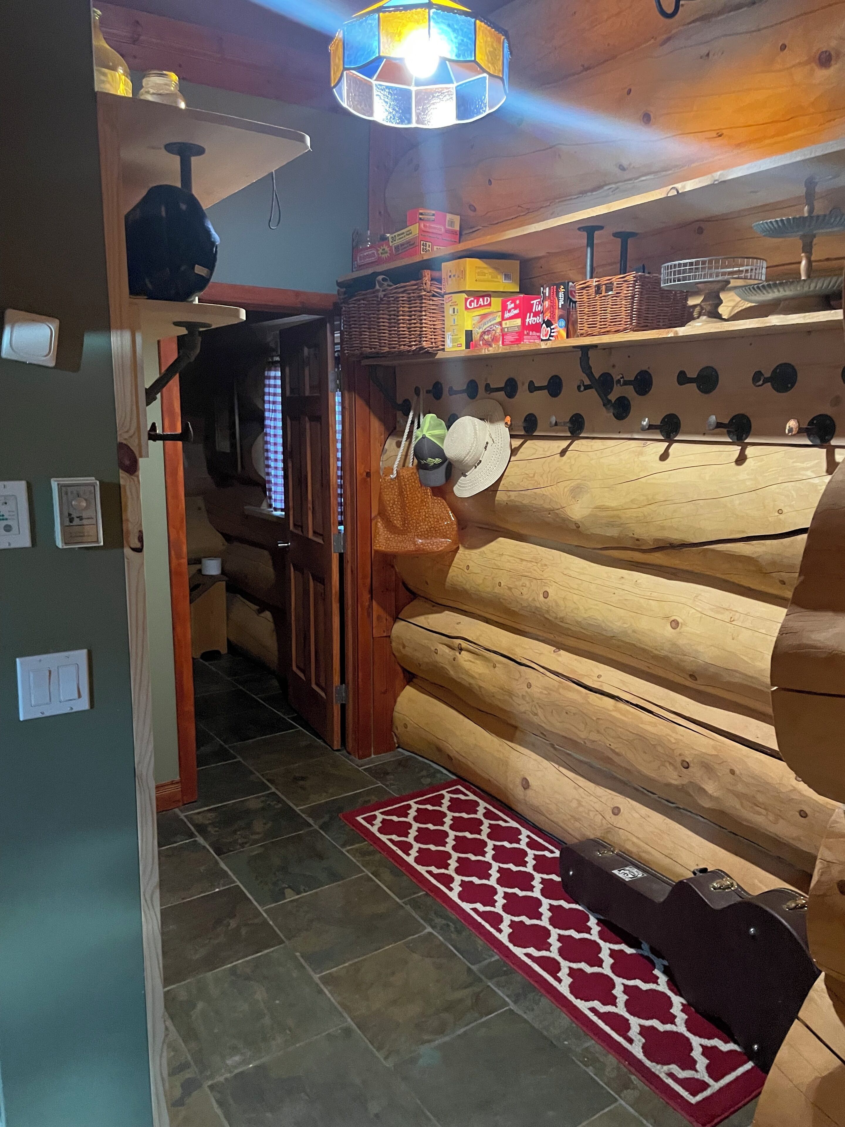 A log cabin interior with a wooden wall, a red patterned rug, and a ceiling light fixture.