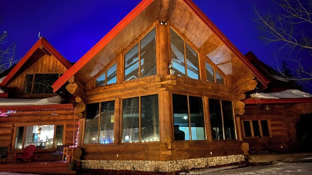 A log cabin with large windows and a stone foundation. - The Lake House (Rimbey)