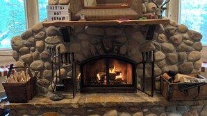 A stone fireplace with a sign above it, a framed picture, and a fire burning inside. - The Lake House (Rimbey)
