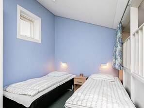 A bedroom with two single beds, a nightstand, a wall-mounted light, and a window with blinds. - 6 Person Holiday Park Home in Faaborg (Faaborg)