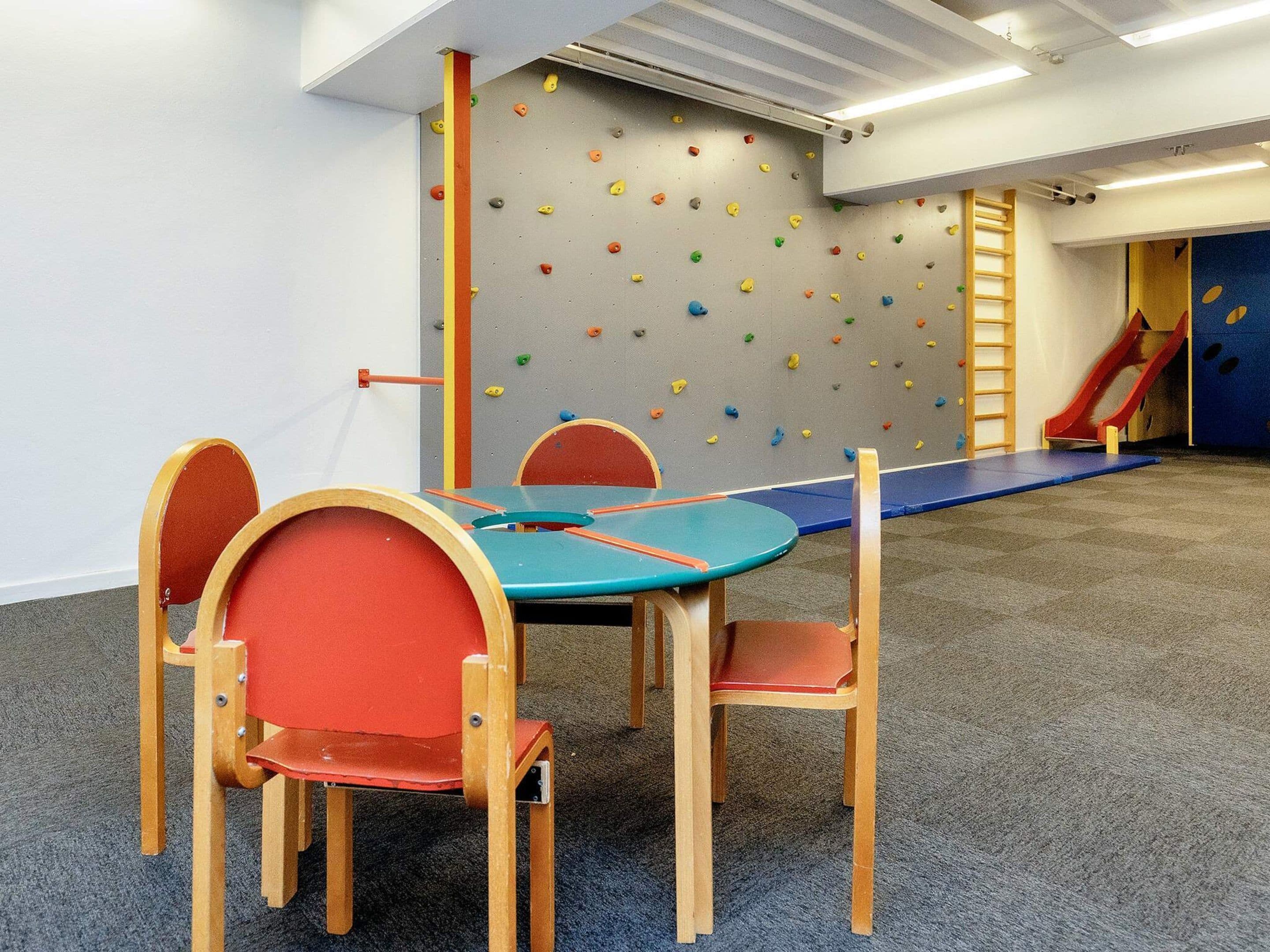 A playroom with a climbing wall, a slide, and a table with chairs.