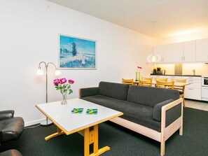 A modern living room with a gray sofa, a small white table with a vase of flowers, and a painting of a snowy landscape. - 6 Person Holiday Park Home in Faaborg (Faaborg)