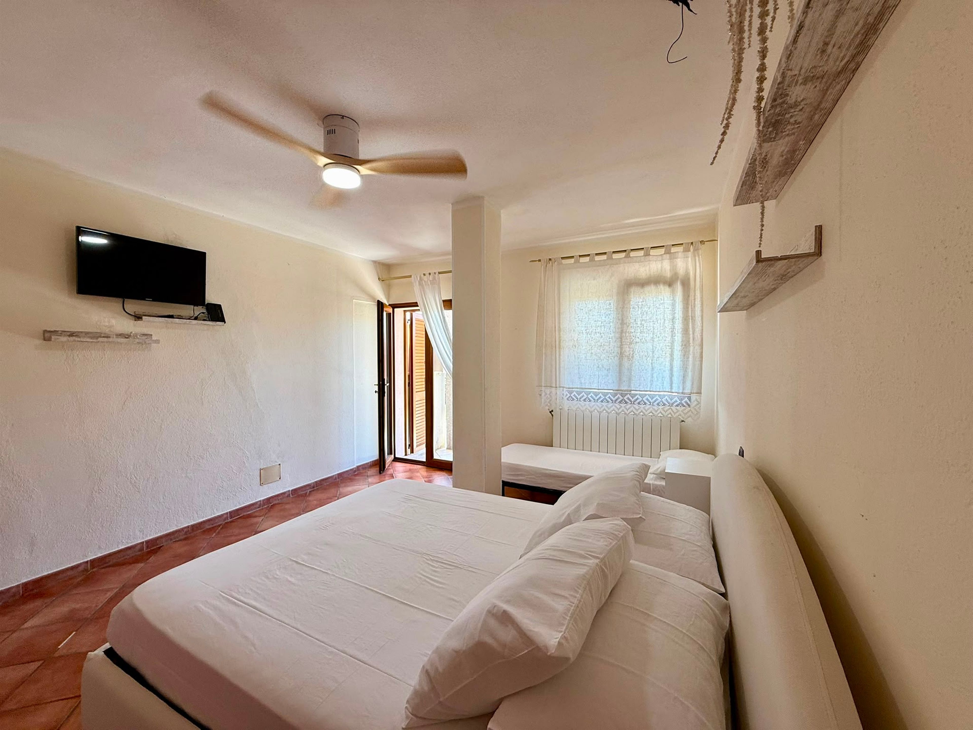 A bedroom with a bed, a ceiling fan, a TV, and a window with curtains.