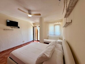 A bedroom with a bed, a ceiling fan, a TV, and a window with curtains. - Villa Olbia surrounded by greenery.Perfect mix of peace and the sea Sardegna (Osseddu)