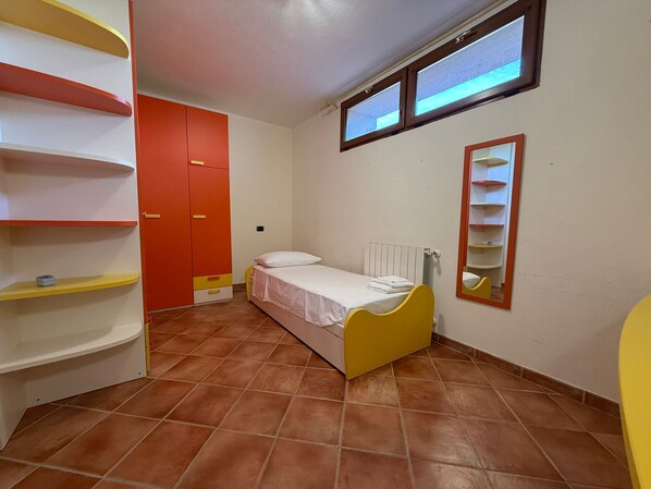 A small, compact room with a bed, a wardrobe, and a shelf unit.