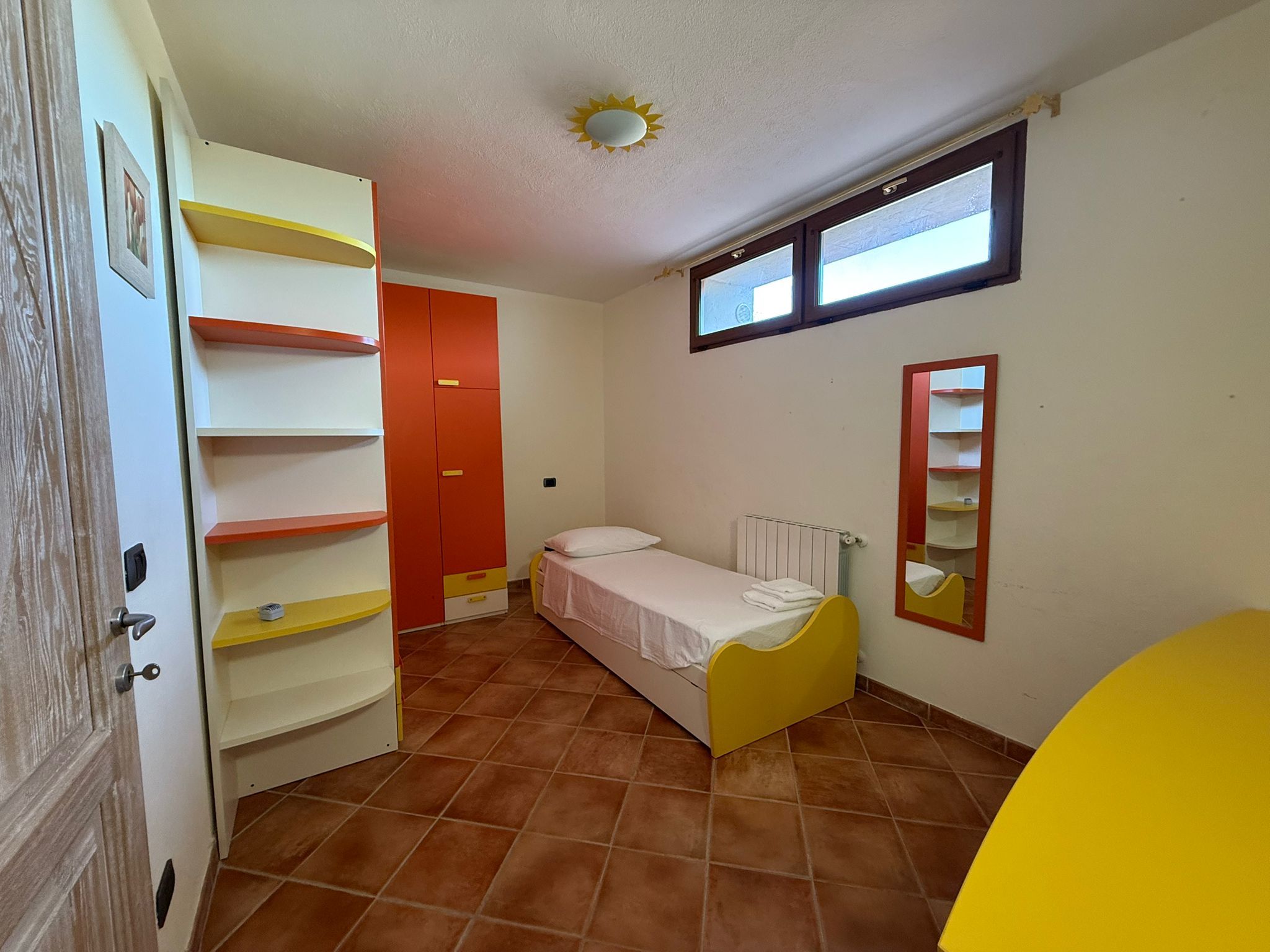 Una camera compatta con un letto singolo, un armadio, un termosifone e una finestra.