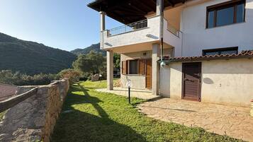 A two-story house with a balcony, a stone wall, and a grassy yard.