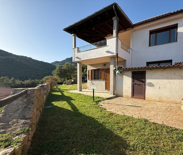 A two-story house with a balcony, a stone wall, and a grassy yard.