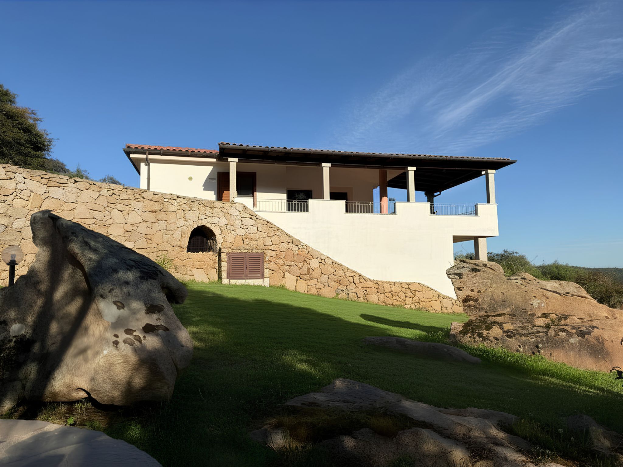 A two-story house with a stone facade, a covered patio, and a grassy lawn.