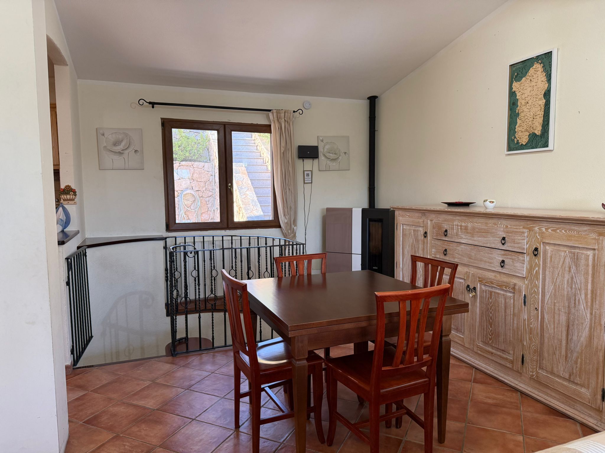Un coin repas avec une table et des chaises en bois, une cuisine avec des placards en bois et une fenêtre avec des rideaux.