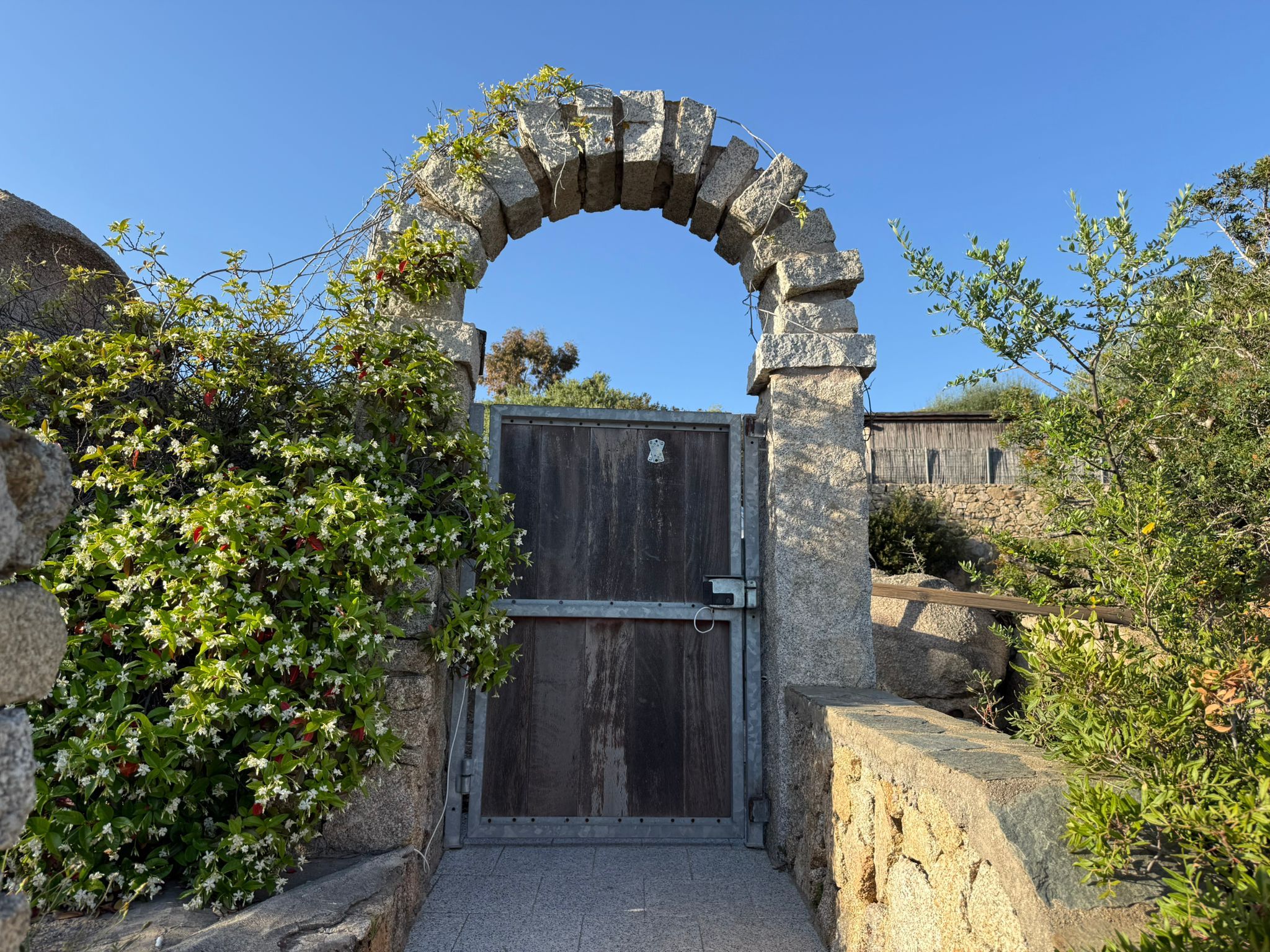 A stone archway leading to a wooden gate, surrounded by greenery.