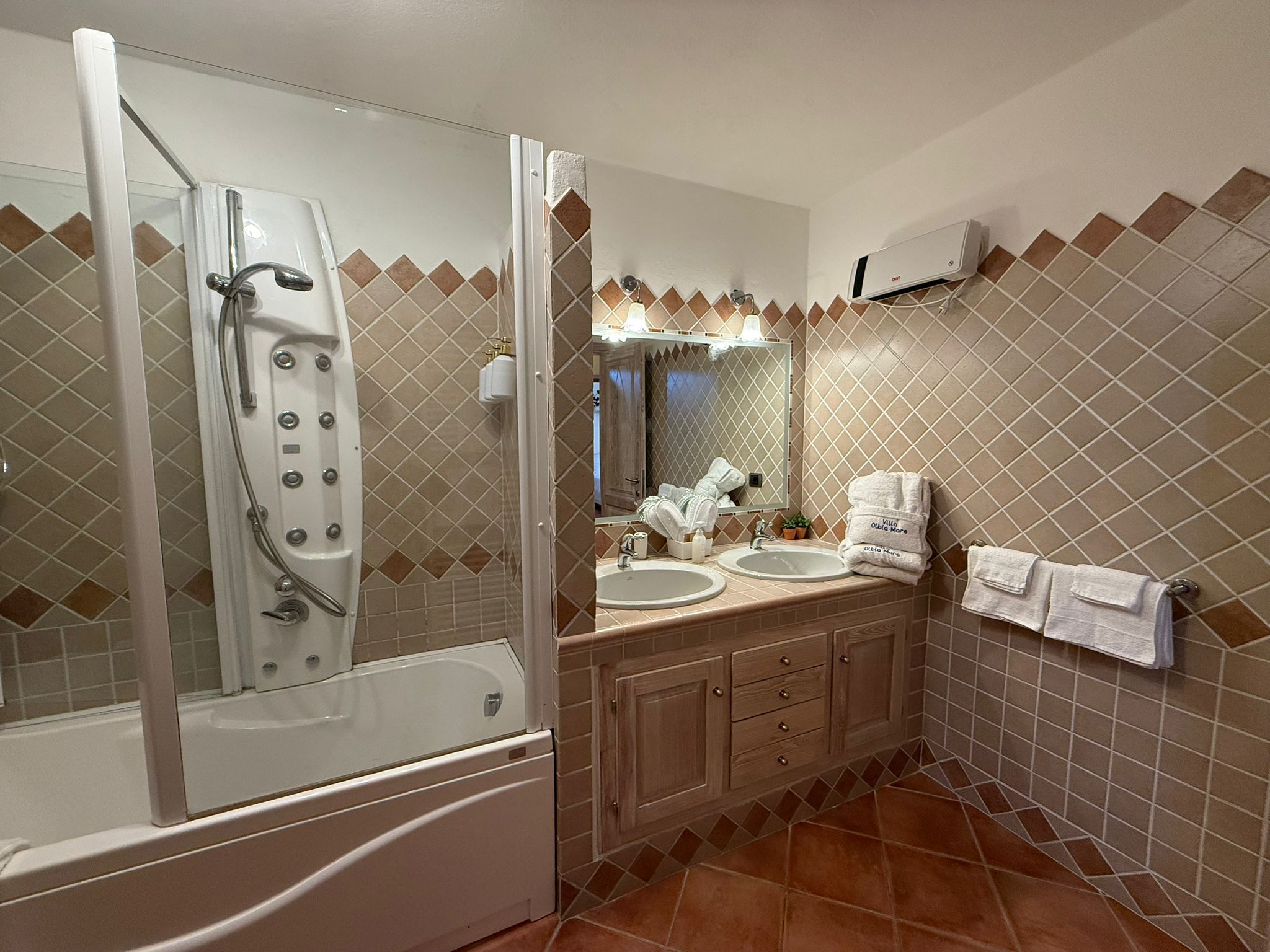 A bathroom with a glass-enclosed shower, two sinks, a mirror, and a towel rack.