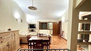 A spacious dining area with a high ceiling, a dining table surrounded by chairs, and a kitchen in the background. - Villa Olbia surrounded by greenery.Perfect mix of peace and the sea Sardegna (Osseddu)